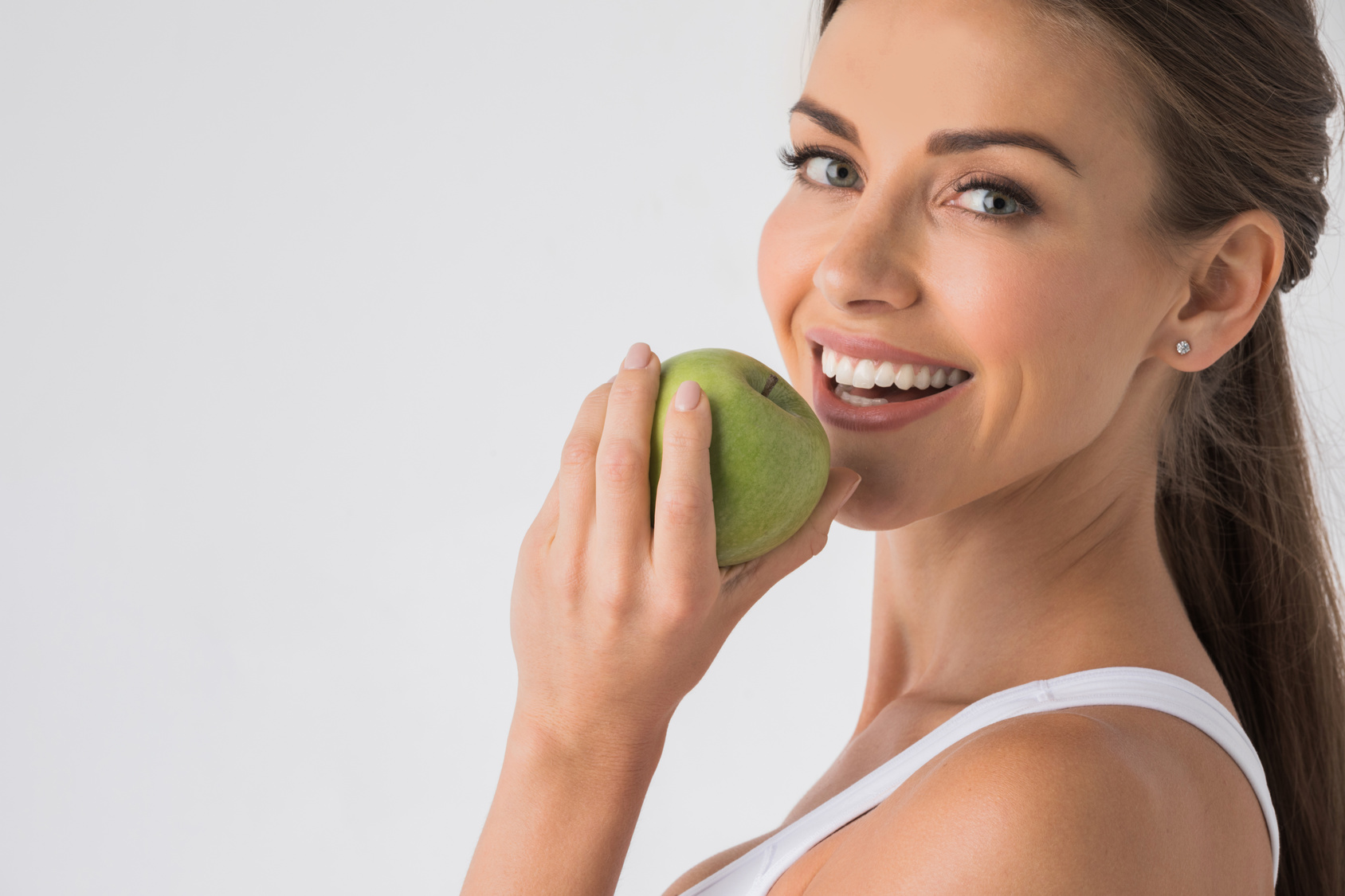 Young woman with healthy teeth smiling and biting green apple