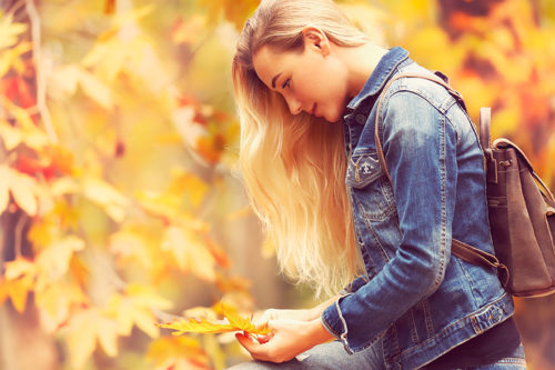 Beautiful model in autumn park, attractive female standing side view and posing over autumnal background, enjoying fall nature